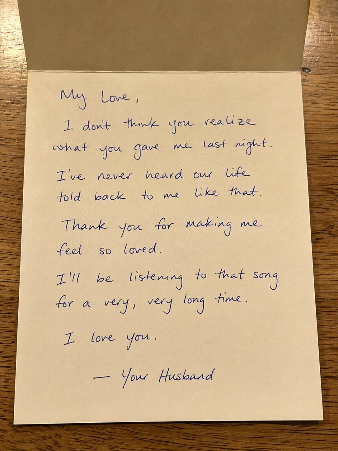 A handwritten note on cream paper, resting in its envelope on a wooden table